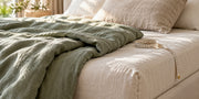 Ivory bedding, a folded sage duvet and a measuring tape beside a mattress